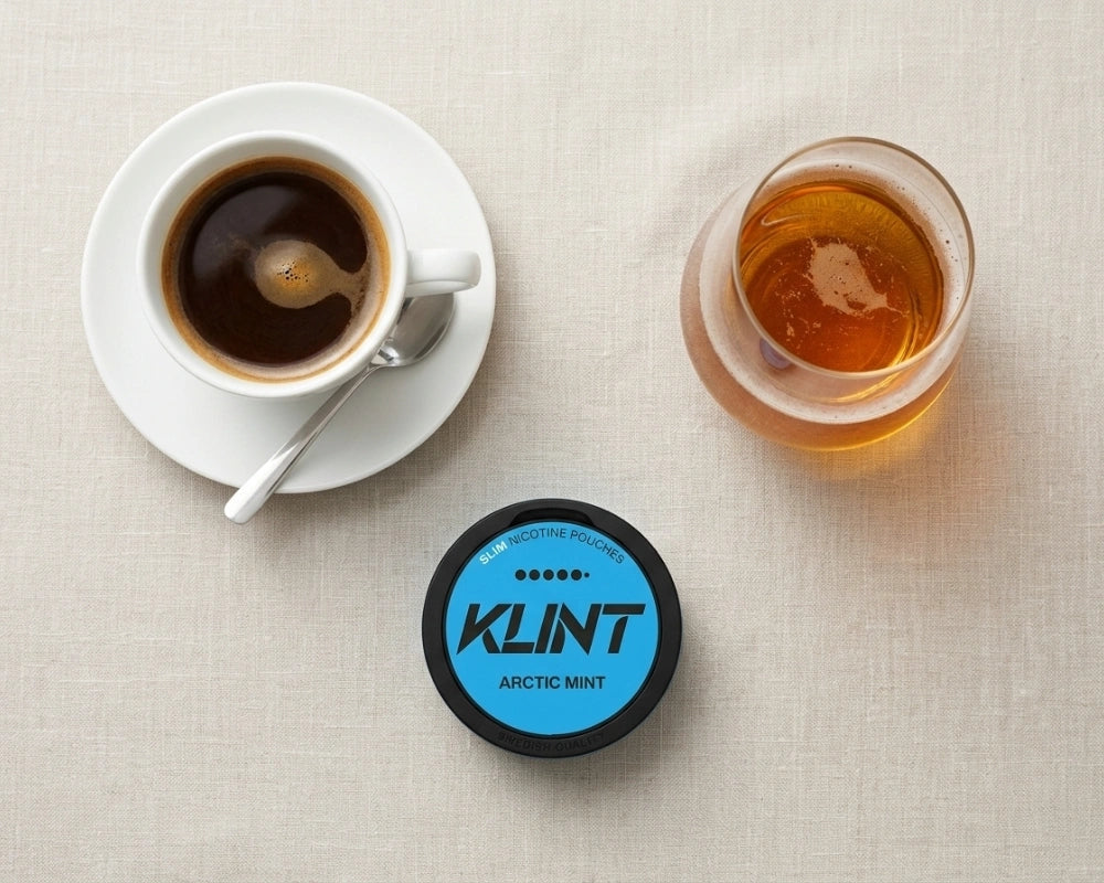 O ceașcă de espresso, un pahar de whisky și o pungă de nicotină KLINT Arctic Mist văzute de sus